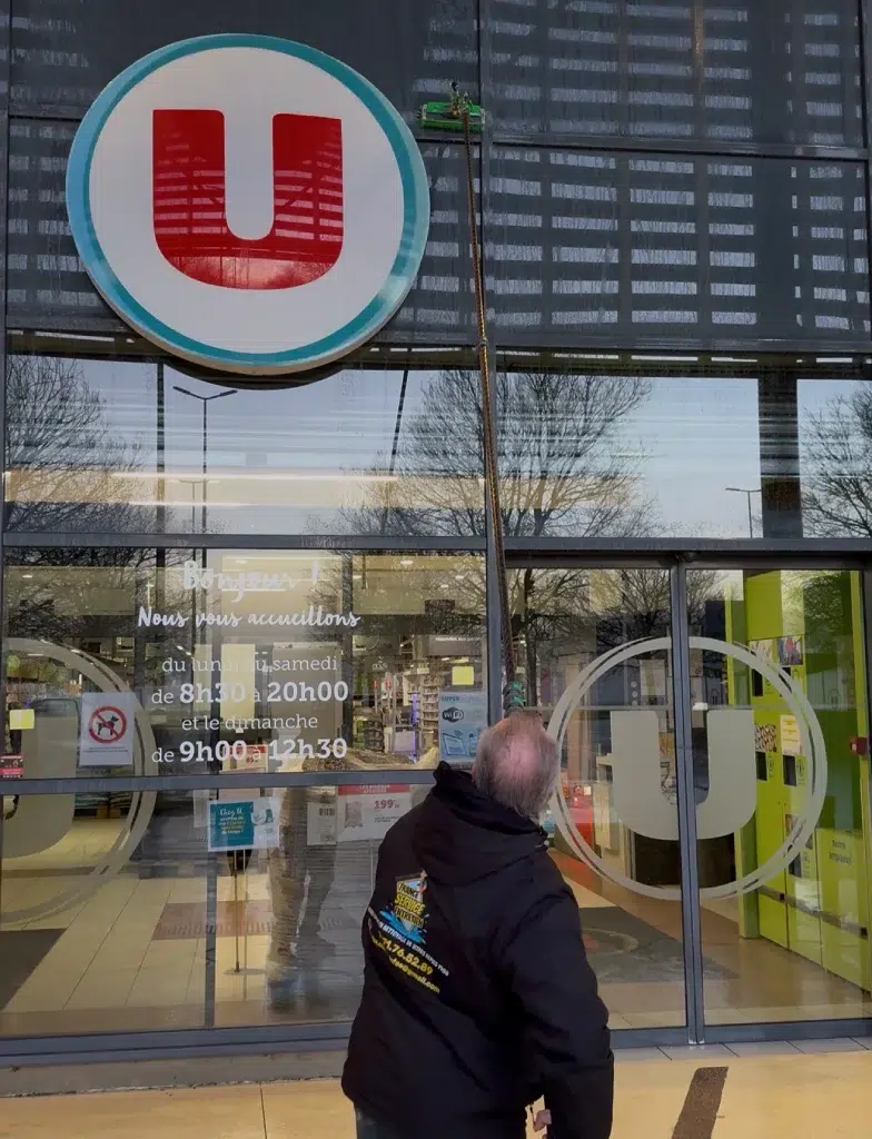 Homme nettoyant la façade d'un magasin Super U